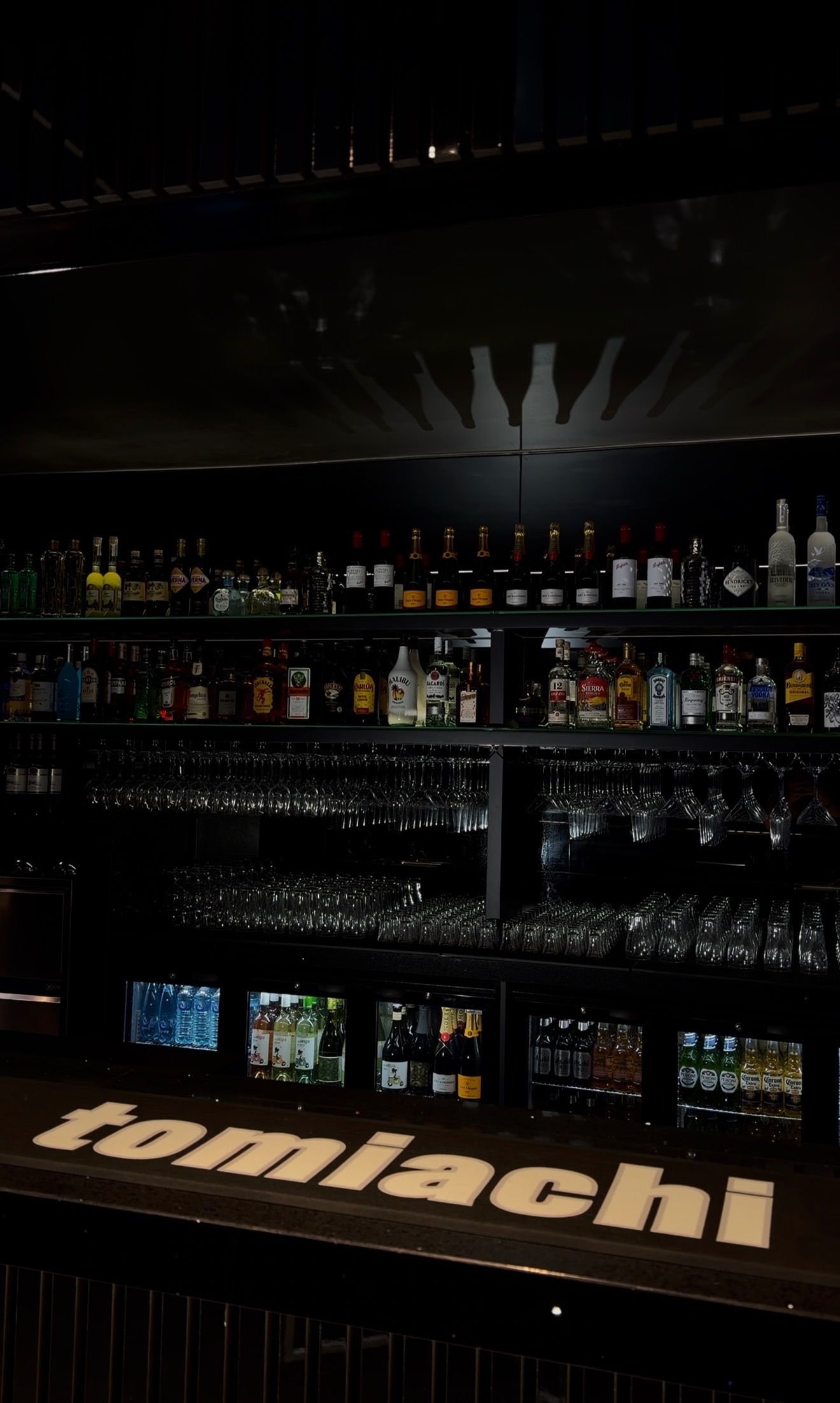 Tomiachi’s built-in black bar stocked with bottles and hanging glassware